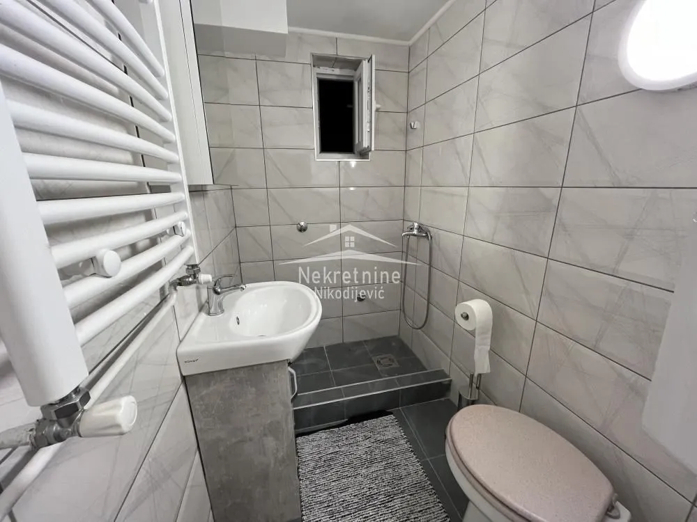 Small tiled bathroom with a walk-in shower area, washbasin and toilet.