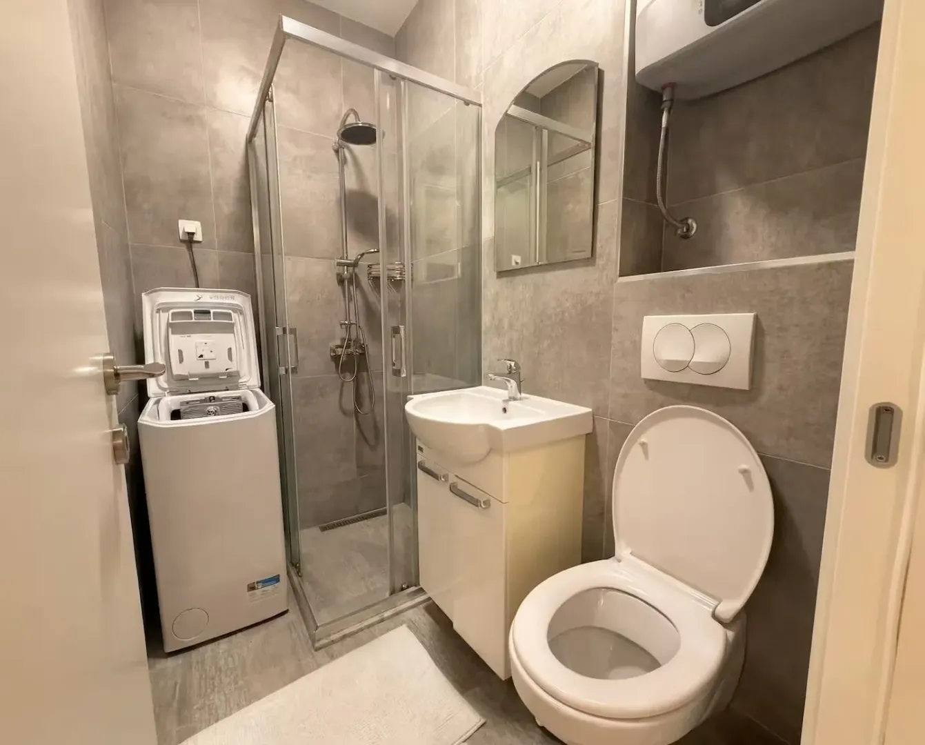 Modern bathroom with a shower cabin, washbasin, toilet, and washing machine.