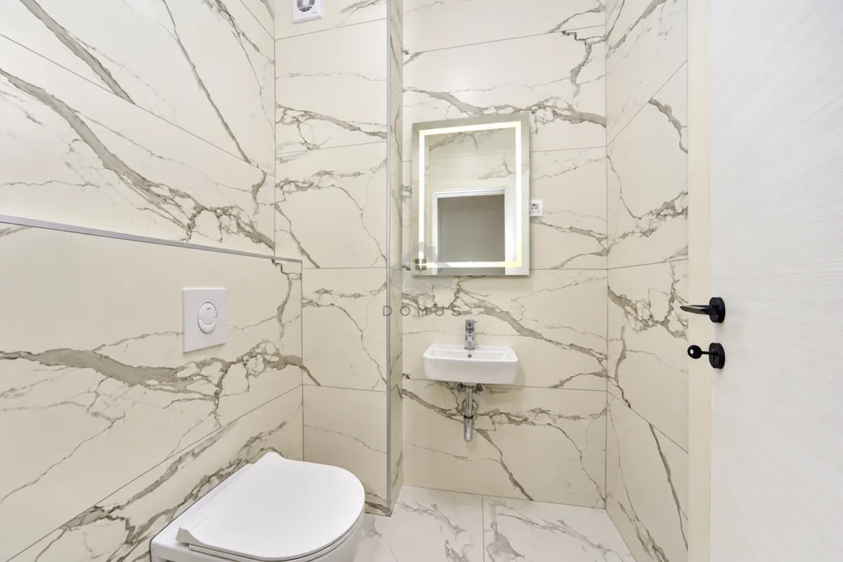 Small bathroom with light marble tiles, a washbasin, and a wall-hung toilet.
