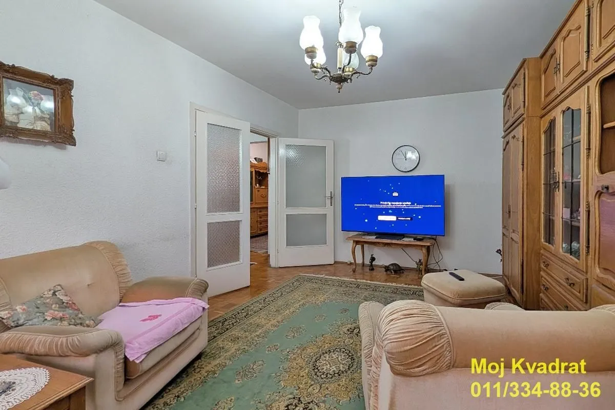 Dnevna soba sa garniturom za sedenje, televizorom i drvenim ormarima.