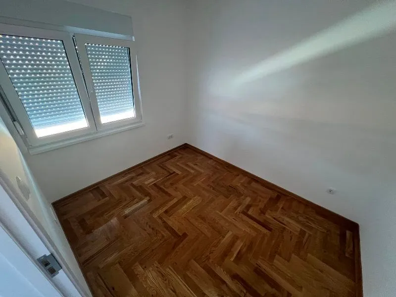 Prazna soba sa parketom i prozorom sa roletnama.