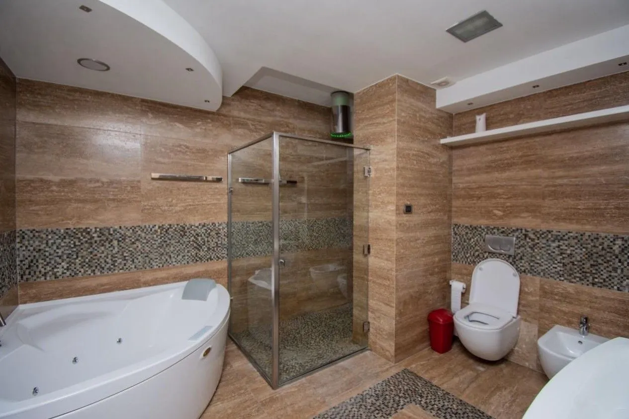 Moderne kupatilo opremljeno kadom, tuš kabinom, sanitarijama i bež keramičkim pločicama.
