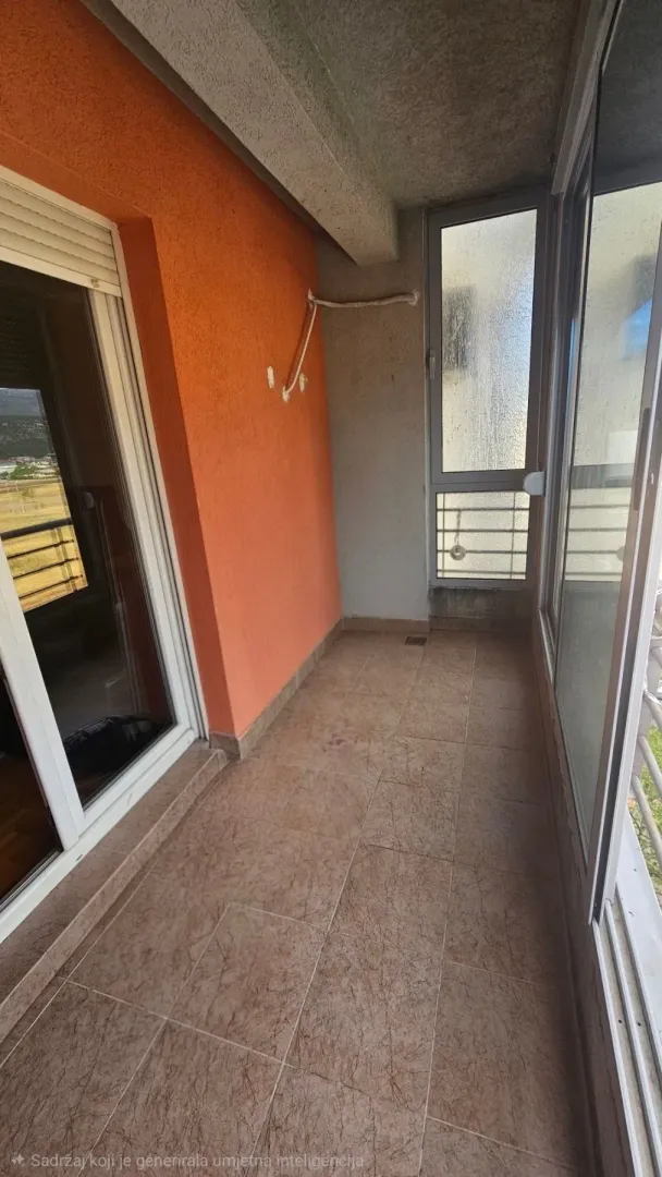 Zastakljeni balkon sa keramičkim pločicama i narandžastim zidom.