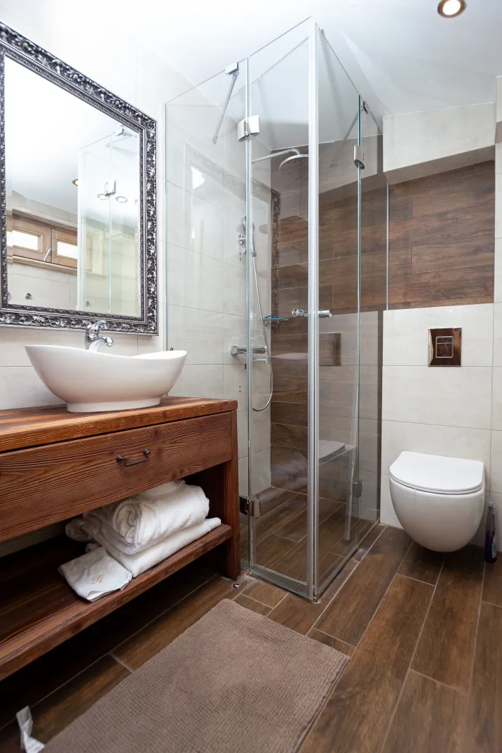 Modernly equipped bathroom with wooden elements, a walk-in shower, and a wall-mounted toilet.