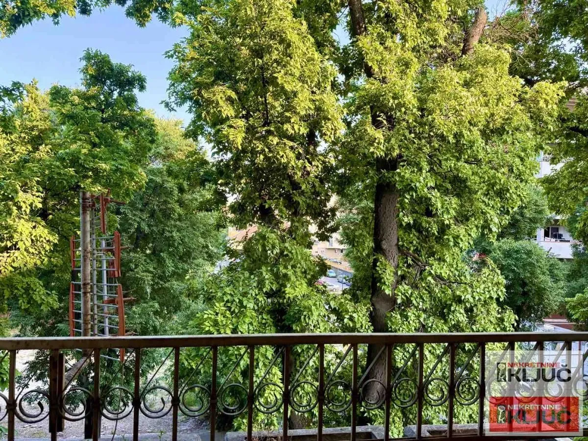 Pogled sa balkona na zelene krošnje drveća i okolinu.
