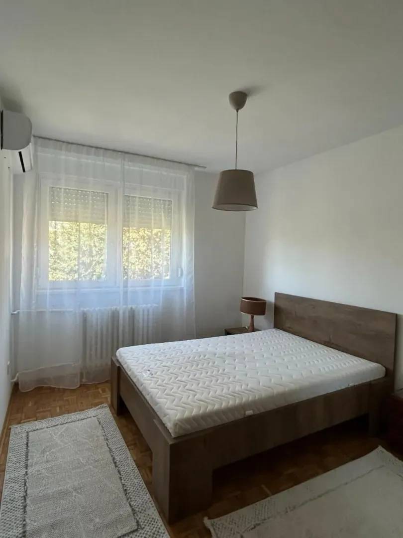 Spavaća soba sa bračnim krevetom, prozorom i klima uređajem.
