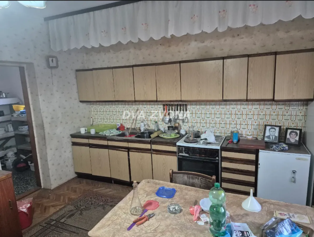 Starija kuhinja sa drvenim elementima, šporetom i trpezarijskim stolom u prvom planu.