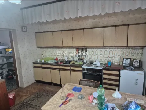 Starija kuhinja sa drvenim elementima, šporetom i trpezarijskim stolom u prvom planu. - image 15