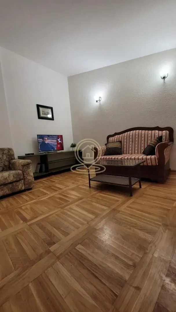 Dnevna soba sa garniturom za sedenje, stočićem i televizorom.