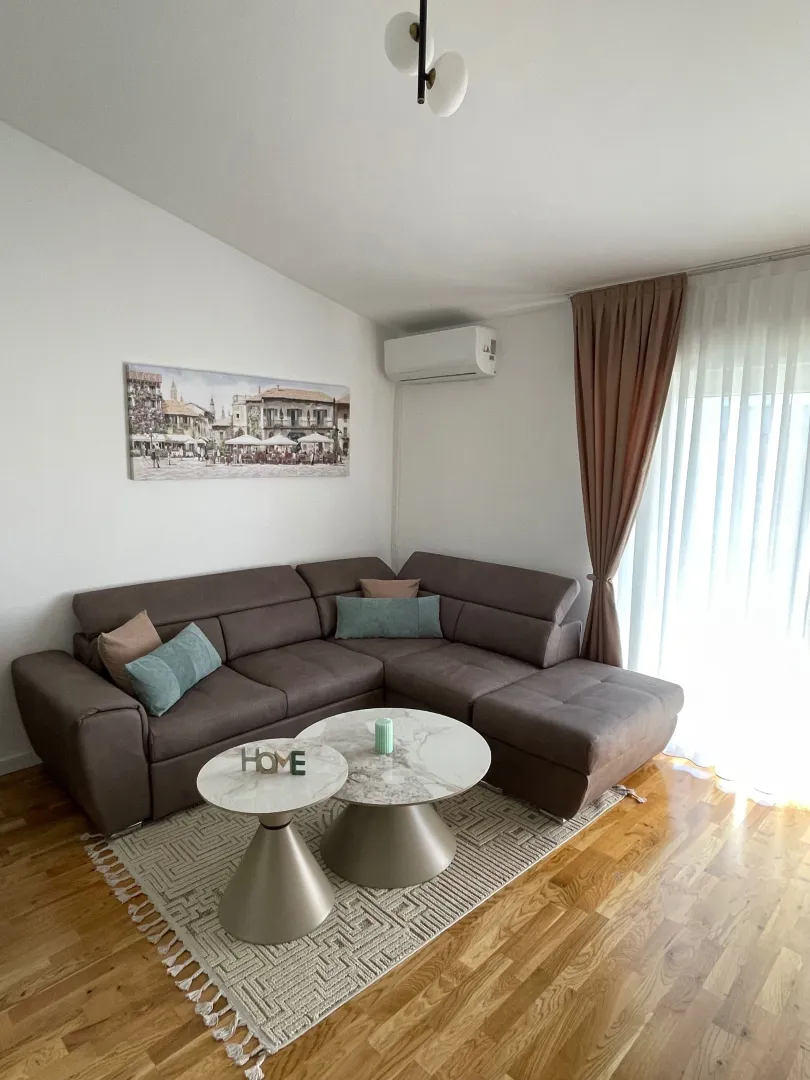 Dnevna soba sa ugaonom garniturom, stočićima i slikom na zidu.