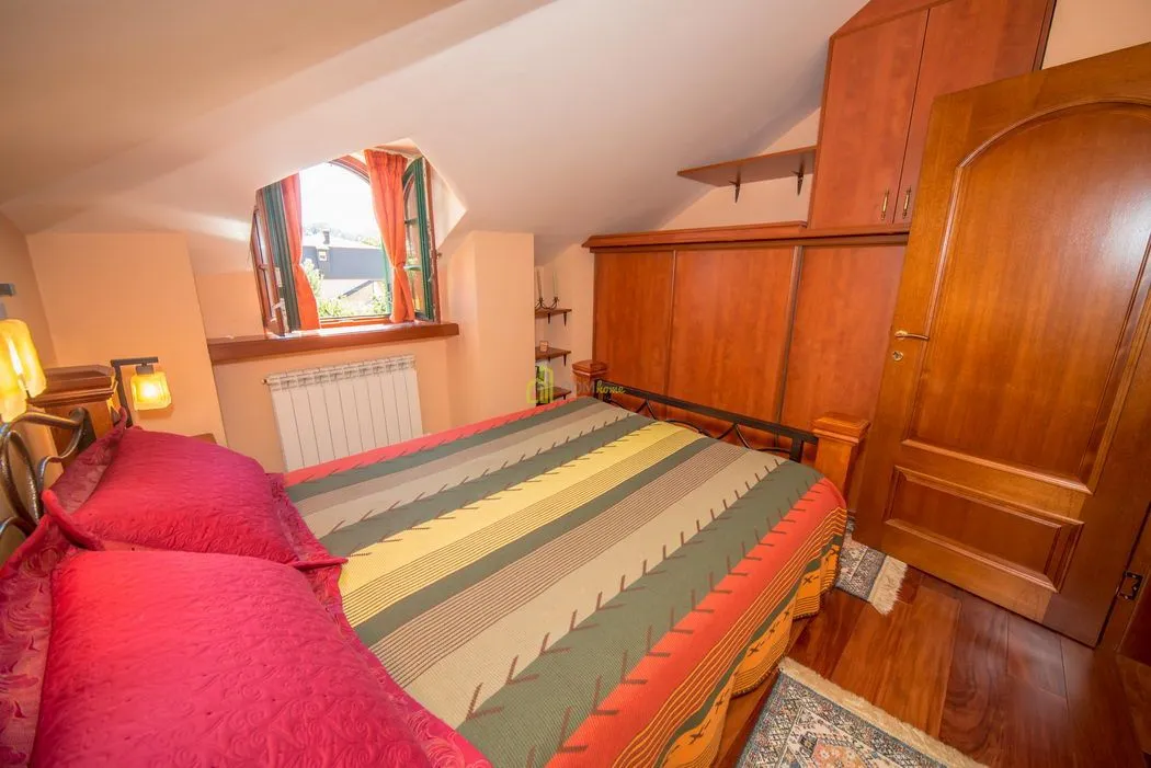Furnished bedroom with a double bed, wooden wardrobes, and a sloped ceiling.