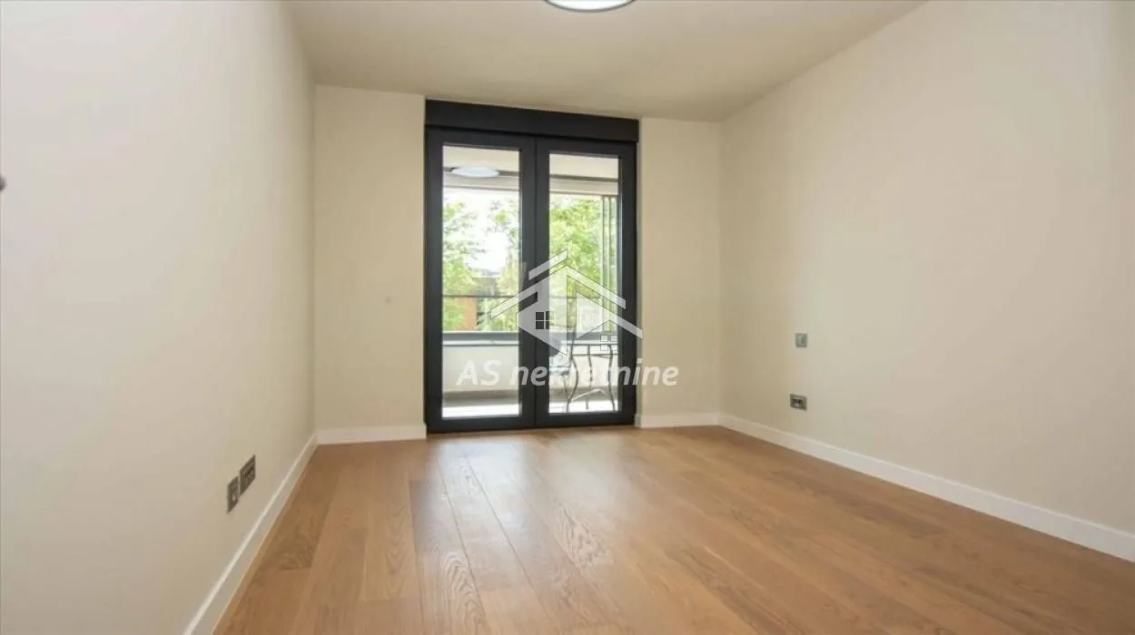Empty room with wooden flooring and balcony doors.