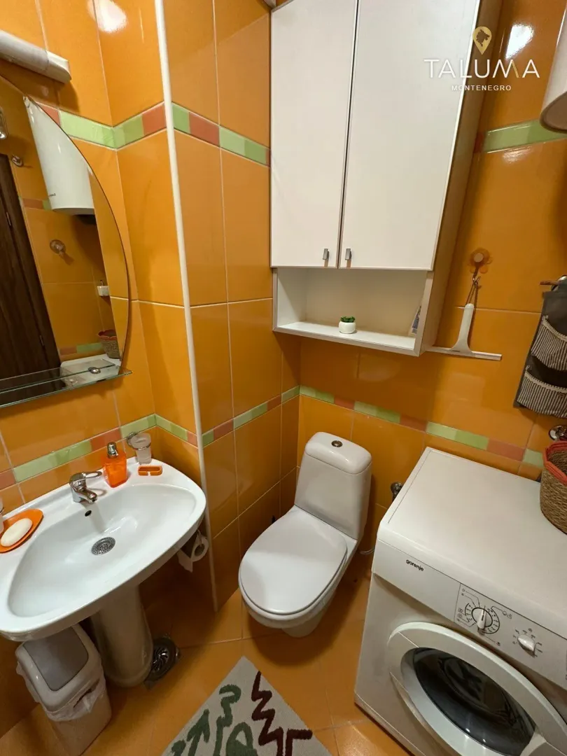 Bathroom with orange tiles, washbasin, toilet bowl and washing machine.