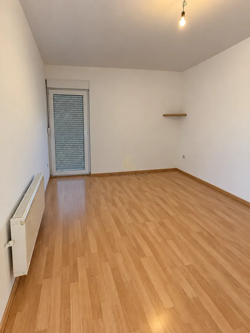 Empty room with white walls, wooden flooring, and balcony door.