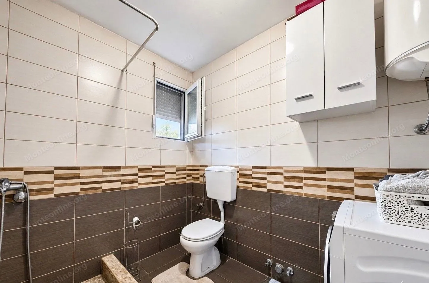 Compact bathroom with light and dark tiles, toilet, and washing machine.