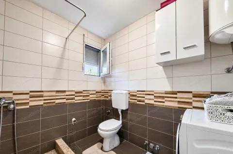 Compact bathroom with light and dark tiles, toilet, and washing machine. - image 7
