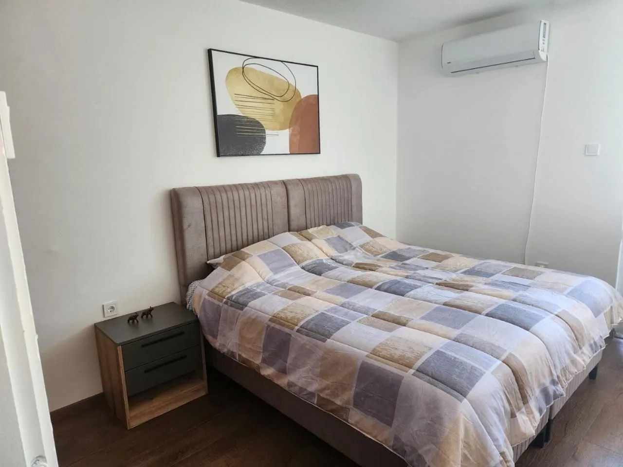 Spavaća soba sa bračnim krevetom, noćnim stočićem i klima uređajem.