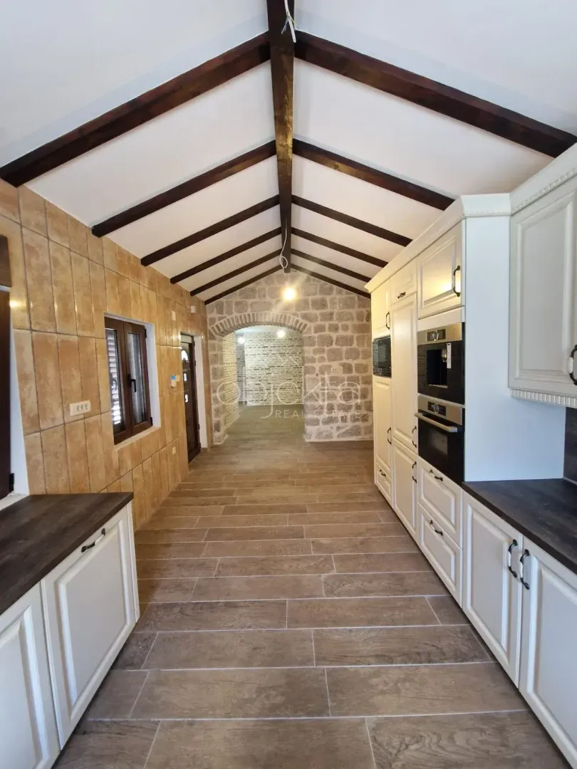 Long kitchen with exposed wooden ceiling beams and a stone wall.