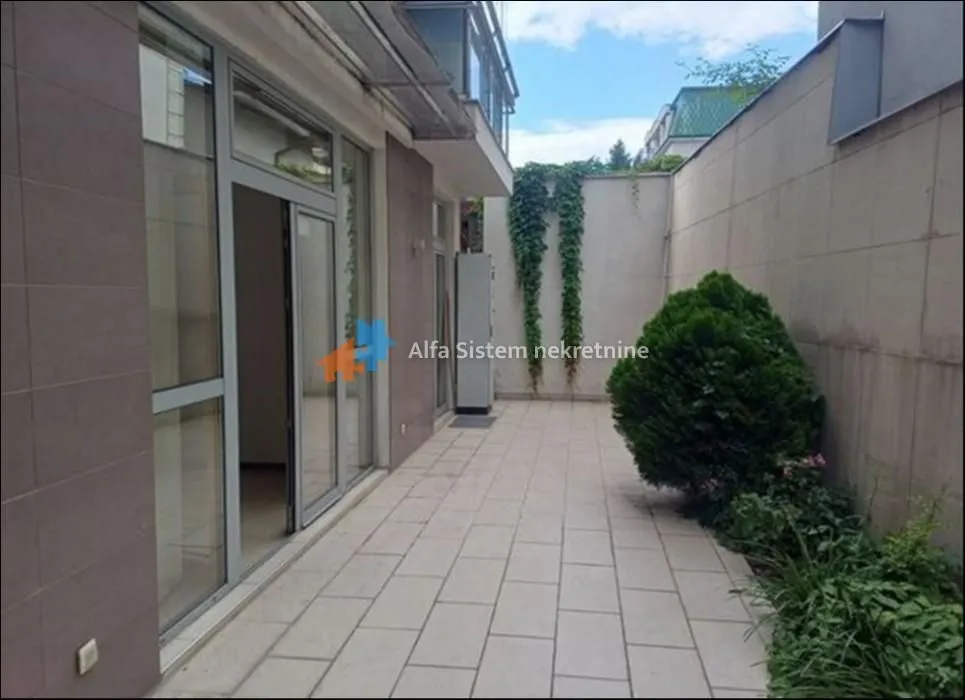Paved courtyard in front of the building entrance with landscaped green areas.