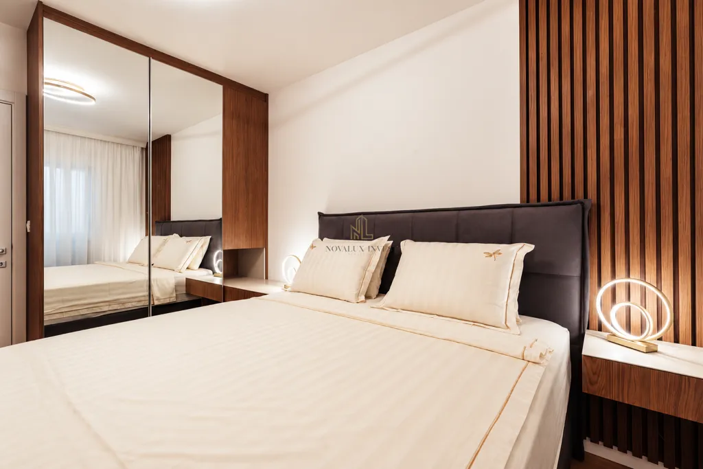 Modern bedroom with a double bed, built-in mirrored wardrobe, and wooden wall panels.