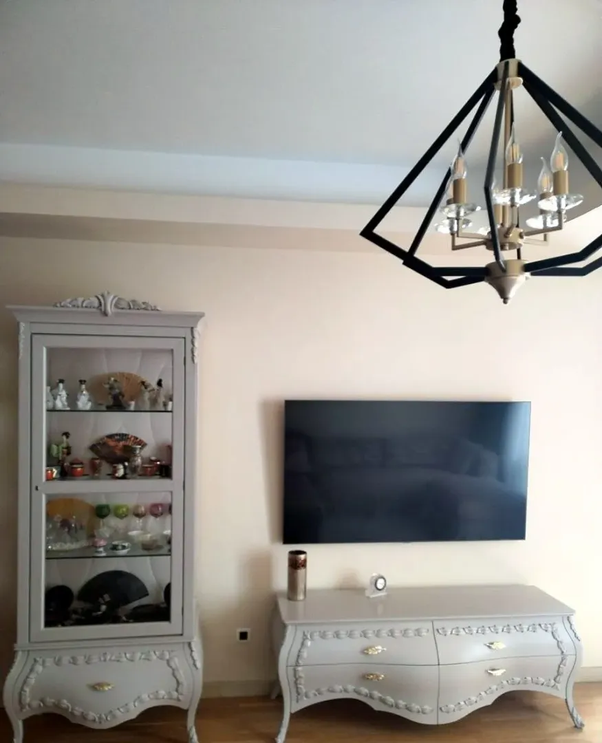 Living room with a TV, chest of drawers, display cabinet, and chandelier.