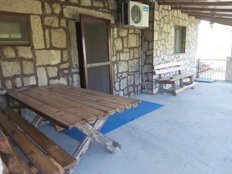Pokrivena terasa sa kamenom fasadom i drvenim stolom sa klupama. - image 4