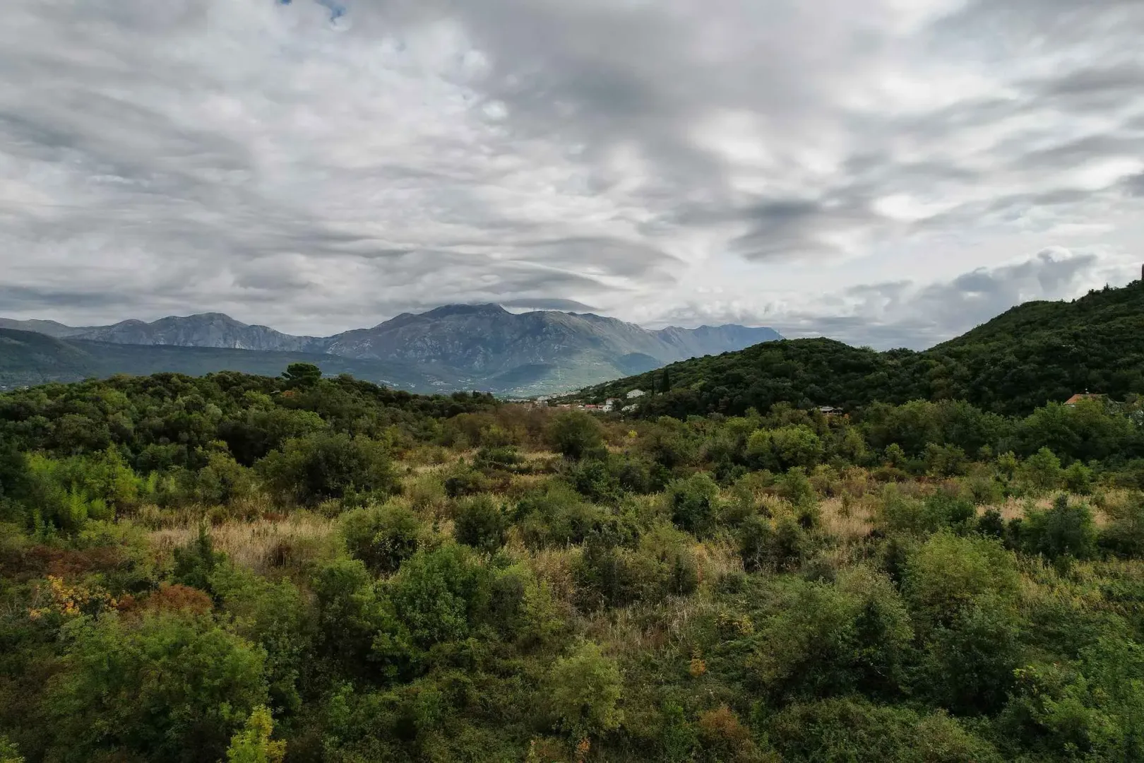 Pogled na zelena brda i planinske vrhove pod oblačnim nebom.
