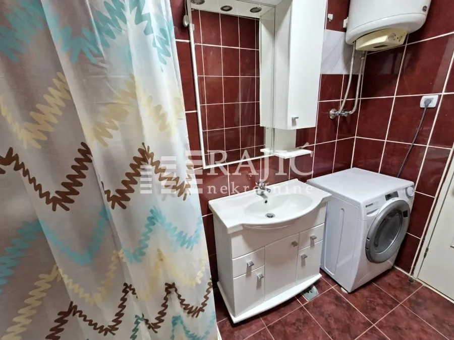 Smaller bathroom with a shower, washbasin, and washing machine.