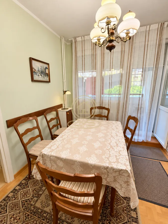Trpezarija sa drvenim stolom, stolicama i lusterom.