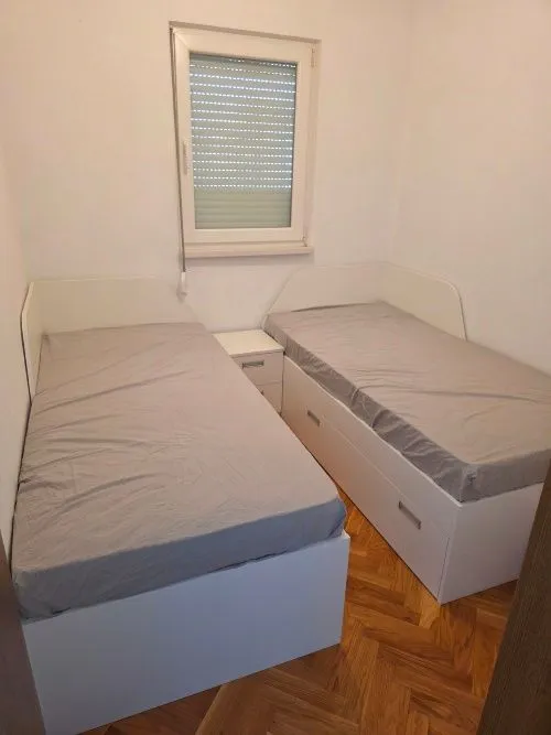 Manja spavaća soba sa dva singl kreveta i prozorom.