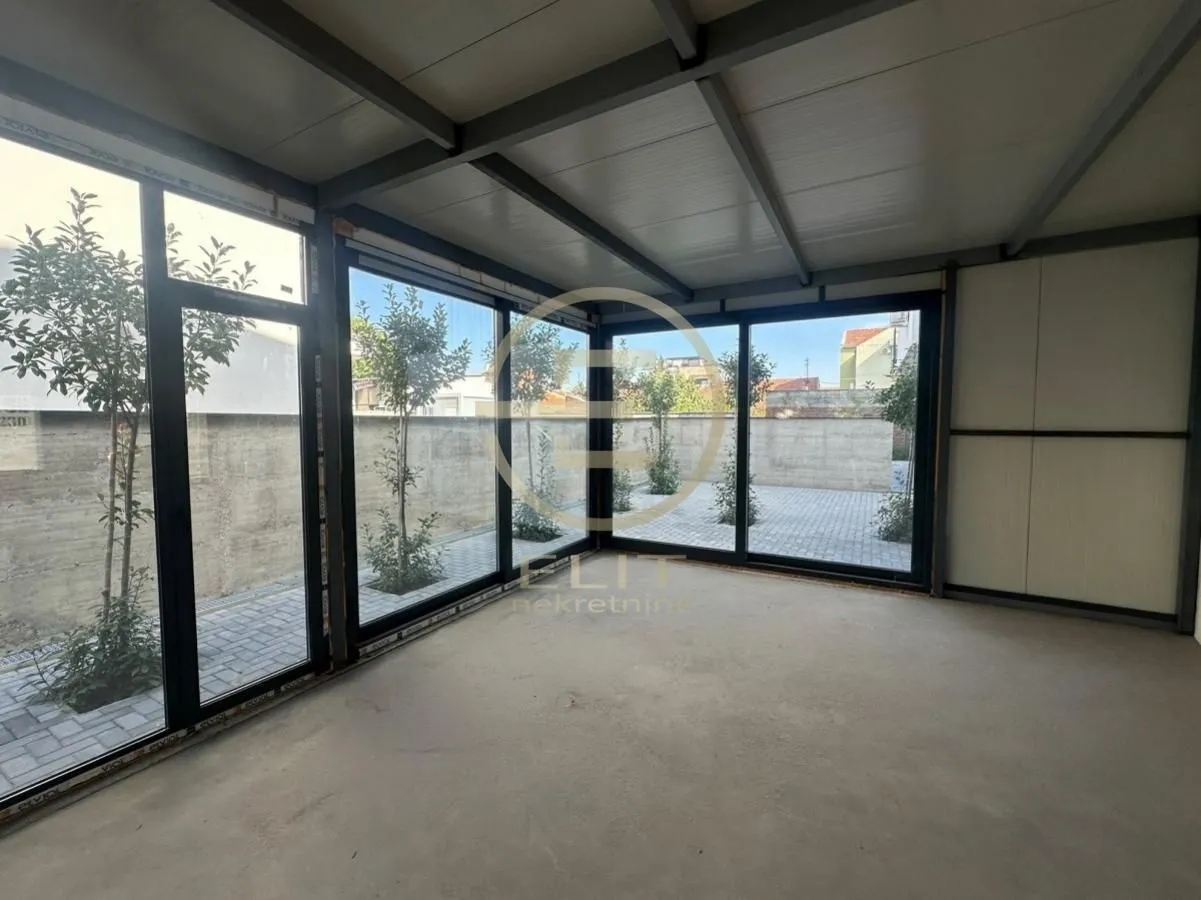 Unfurnished room under construction with large glass surfaces and a view of the paved courtyard.