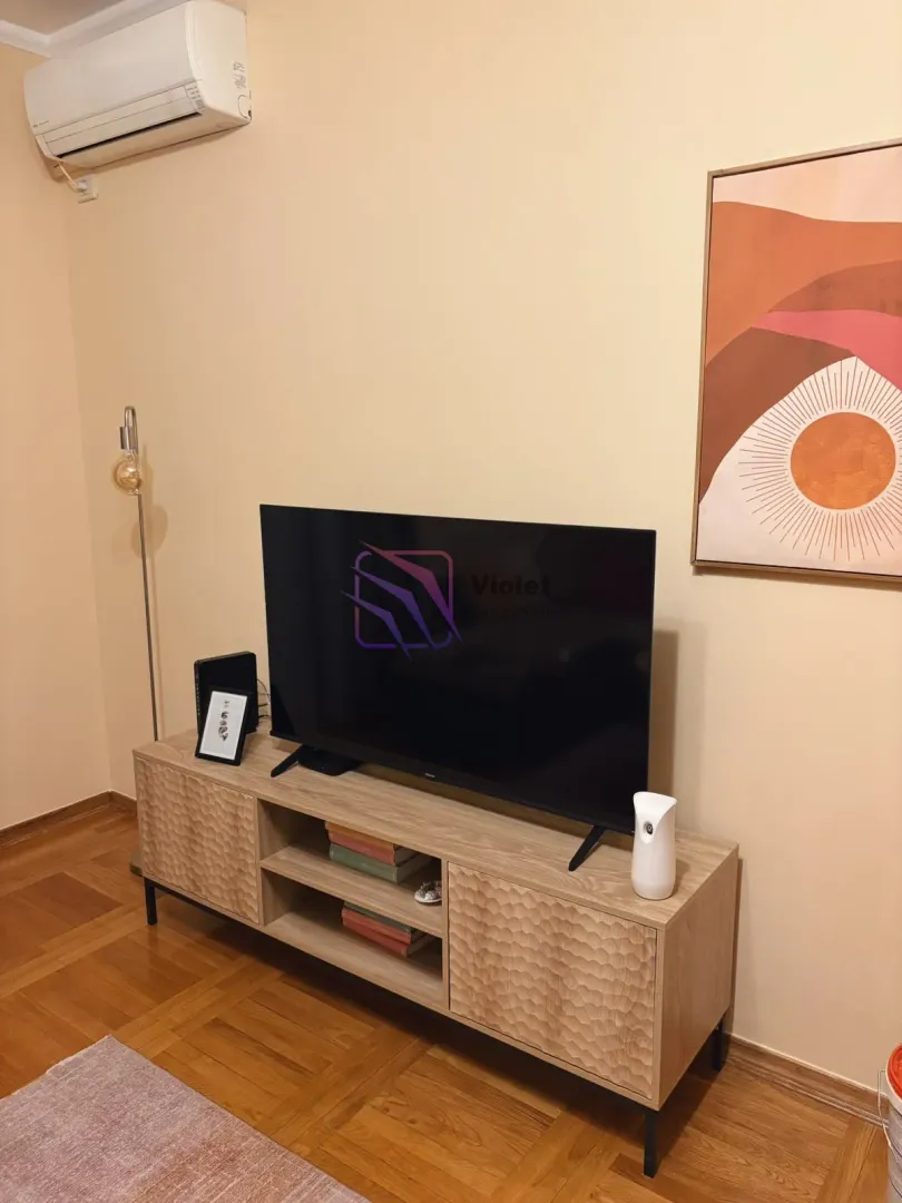 Dnevna soba sa televizorom na komodi i klima uređajem na zidu.