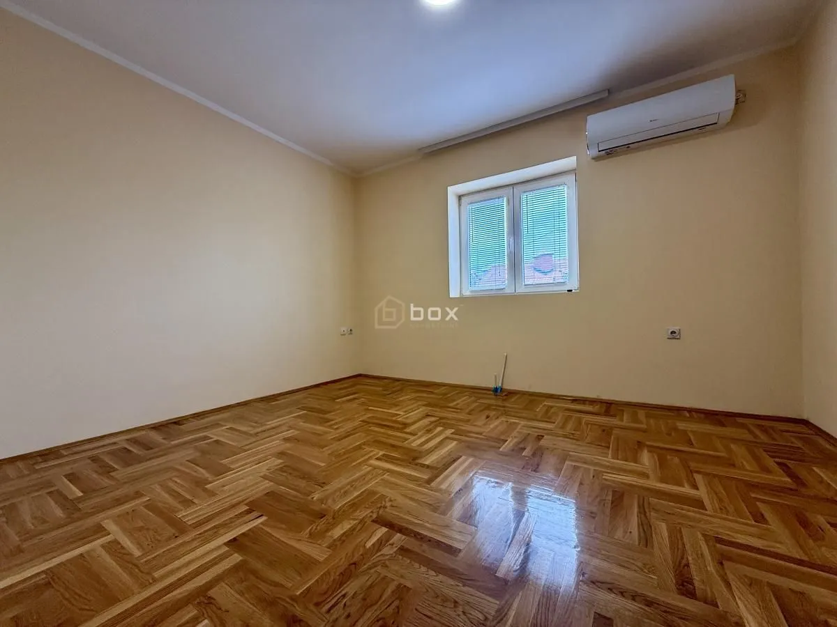Empty room with parquet flooring and an air conditioning unit.