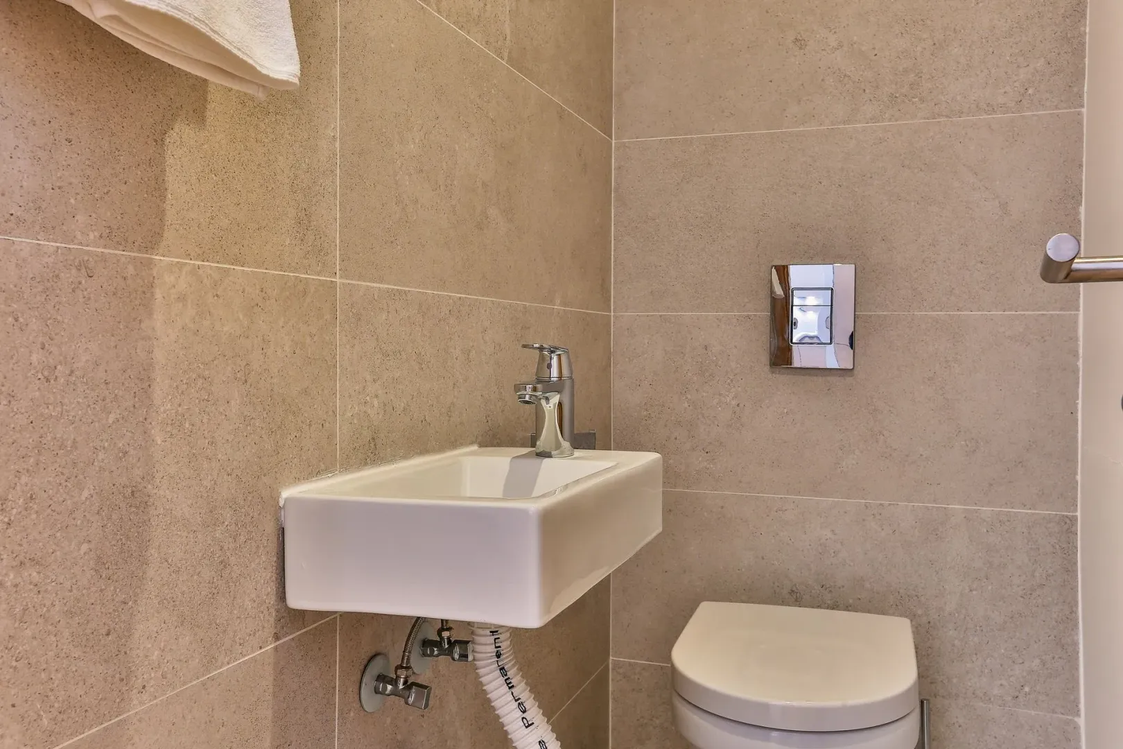 Smaller bathroom with a washbasin and a built-in toilet, tiled in beige ceramic tiles.
