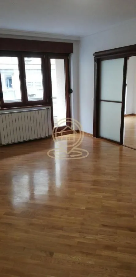 Prazna soba sa drvenim parketom, prozorom i kliznim vratima.