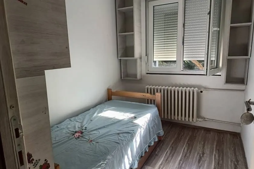 Small bedroom with a single bed, window, and wall shelving unit.