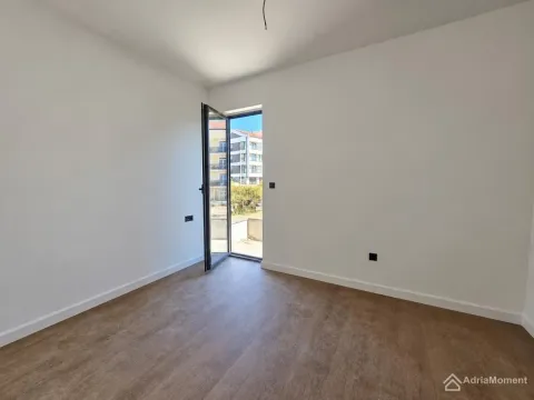 Prazna soba sa bijelim zidovima i drvenim podom, sa otvorenim balkonskim vratima. - image 4