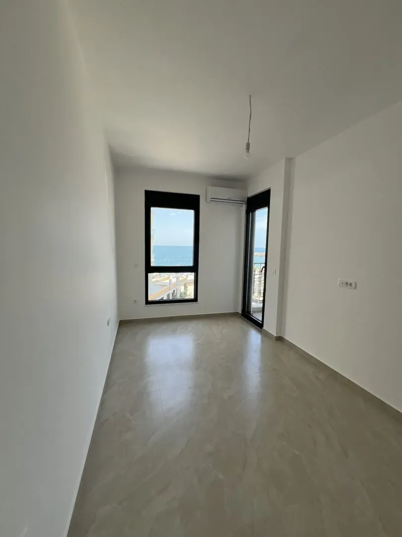 An empty, bright room with a window offering a sea view.