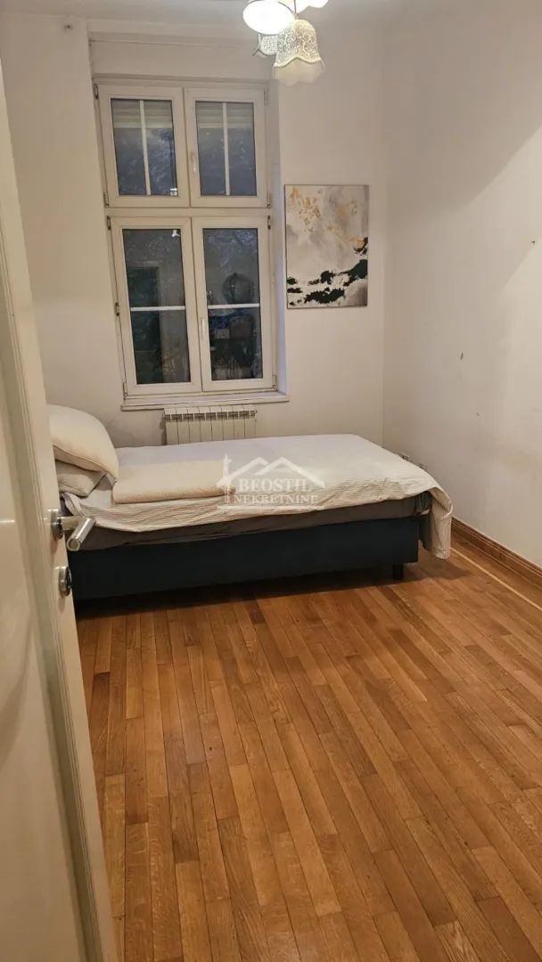 Manja spavaća soba sa krevetom i drvenim podom.