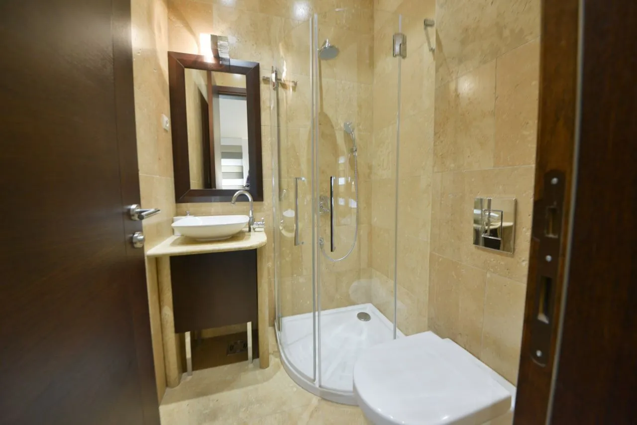 Kupatilo opremljeno tuš kabinom, umivaonikom i WC šoljom obloženo pločicama u boji pijeska.