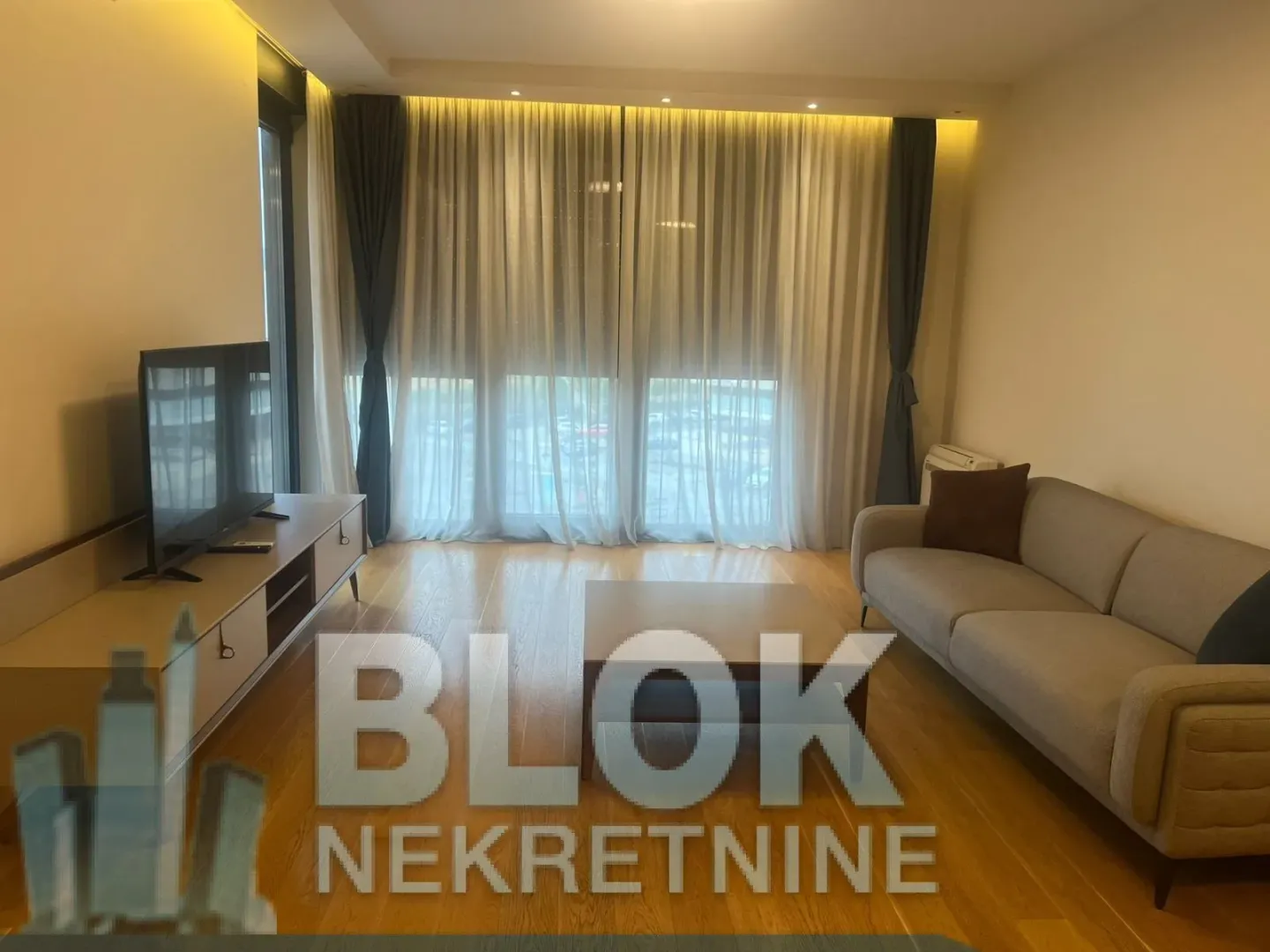 Living room with a sofa, TV, and a large window with curtains.