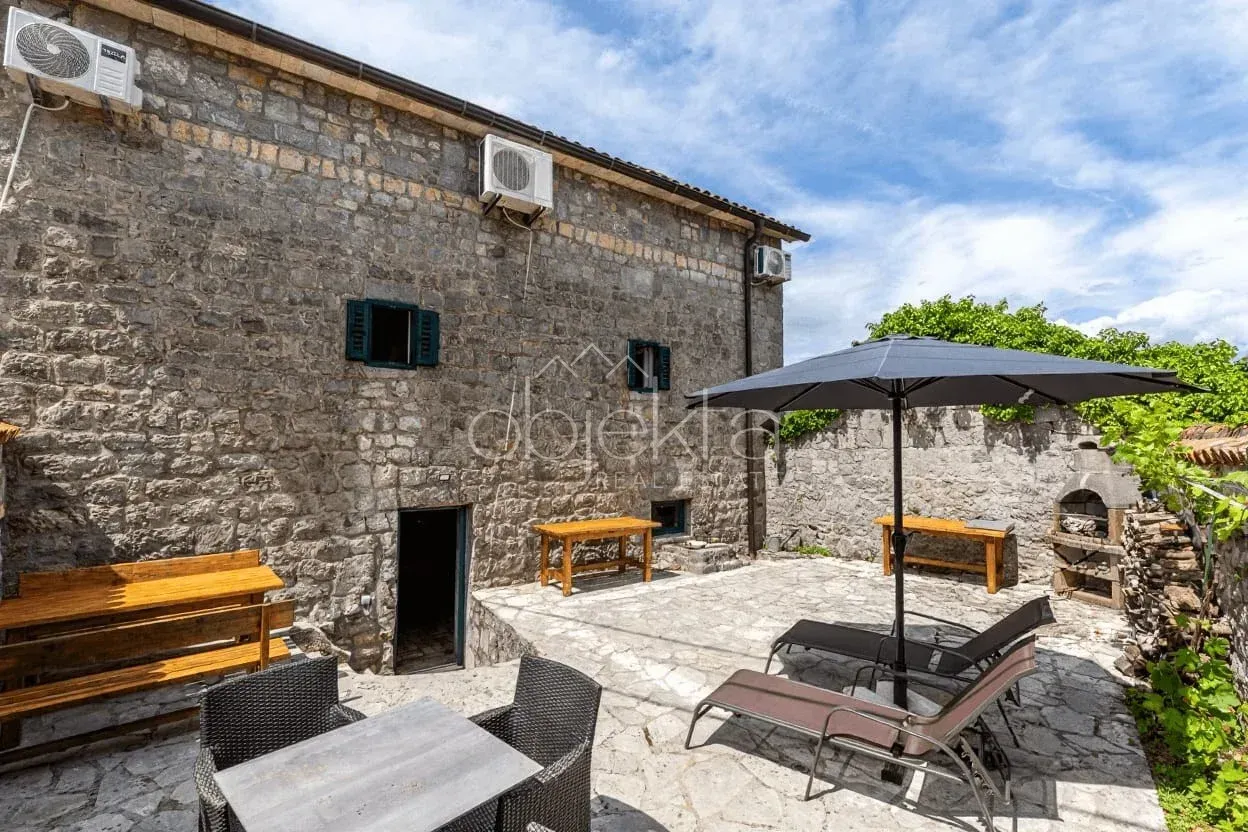 Popločano dvorište tradicionalne kamene kuće sa garniturom za sjedenje i ležaljkama.