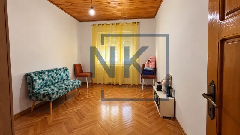 Dnevna soba sa drvenim podom, kaučom i prozorom sa žutim zavjesama.