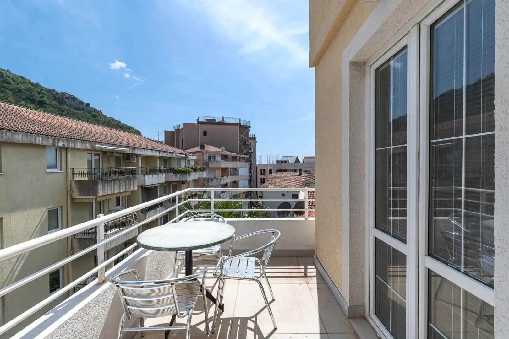 Furnished balcony with a table and chairs and a view of surrounding buildings and a hill.