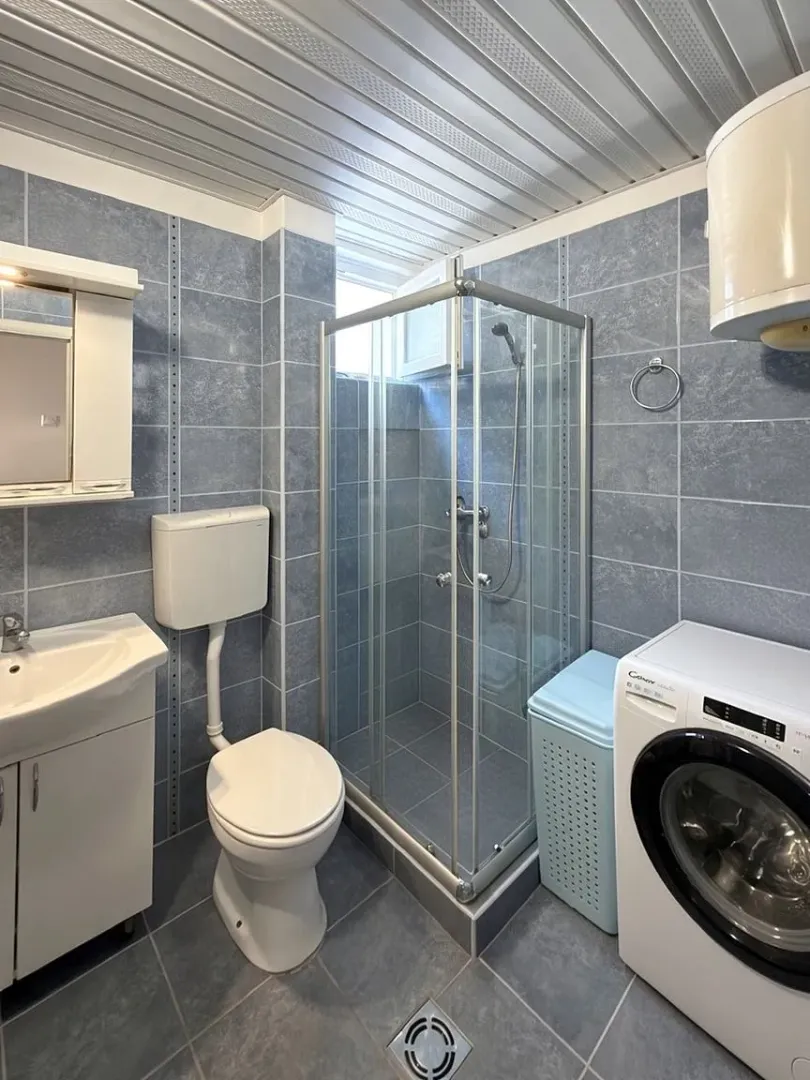 Tiled bathroom featuring a shower cabin, washbasin, toilet, and washing machine.