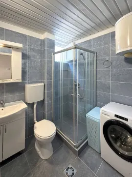Tiled bathroom featuring a shower cabin, washbasin, toilet, and washing machine. - image 2