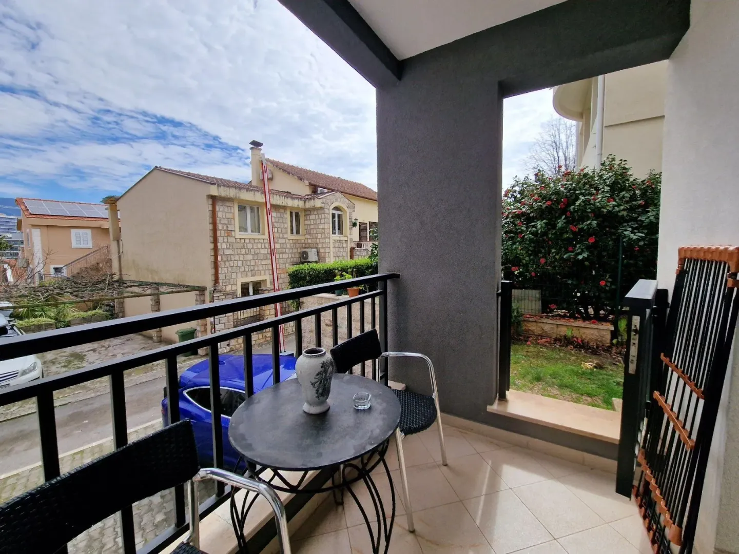 Natkriveni balkon sa garniturom za sjedenje i pogledom na okolne kuće i dvorište.