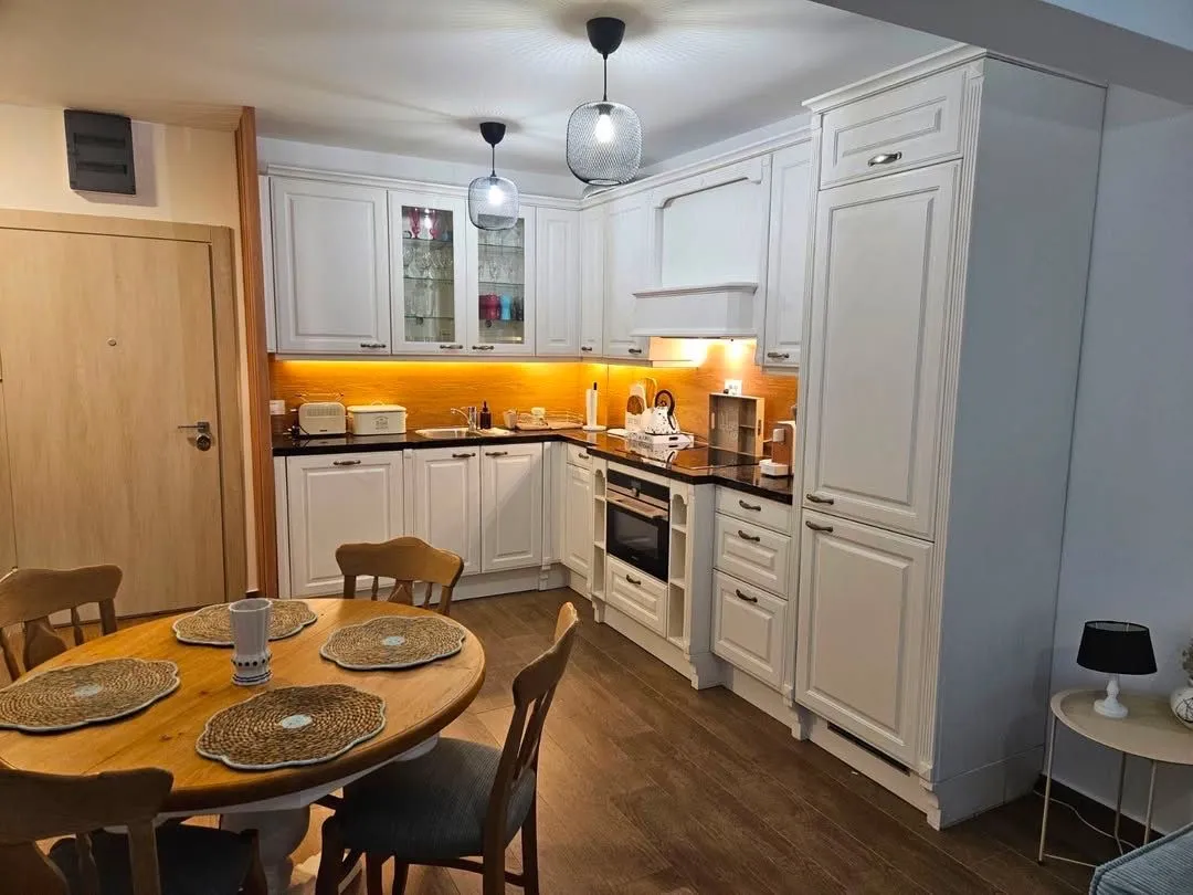 Modern white kitchen with a dining table and wooden floor.