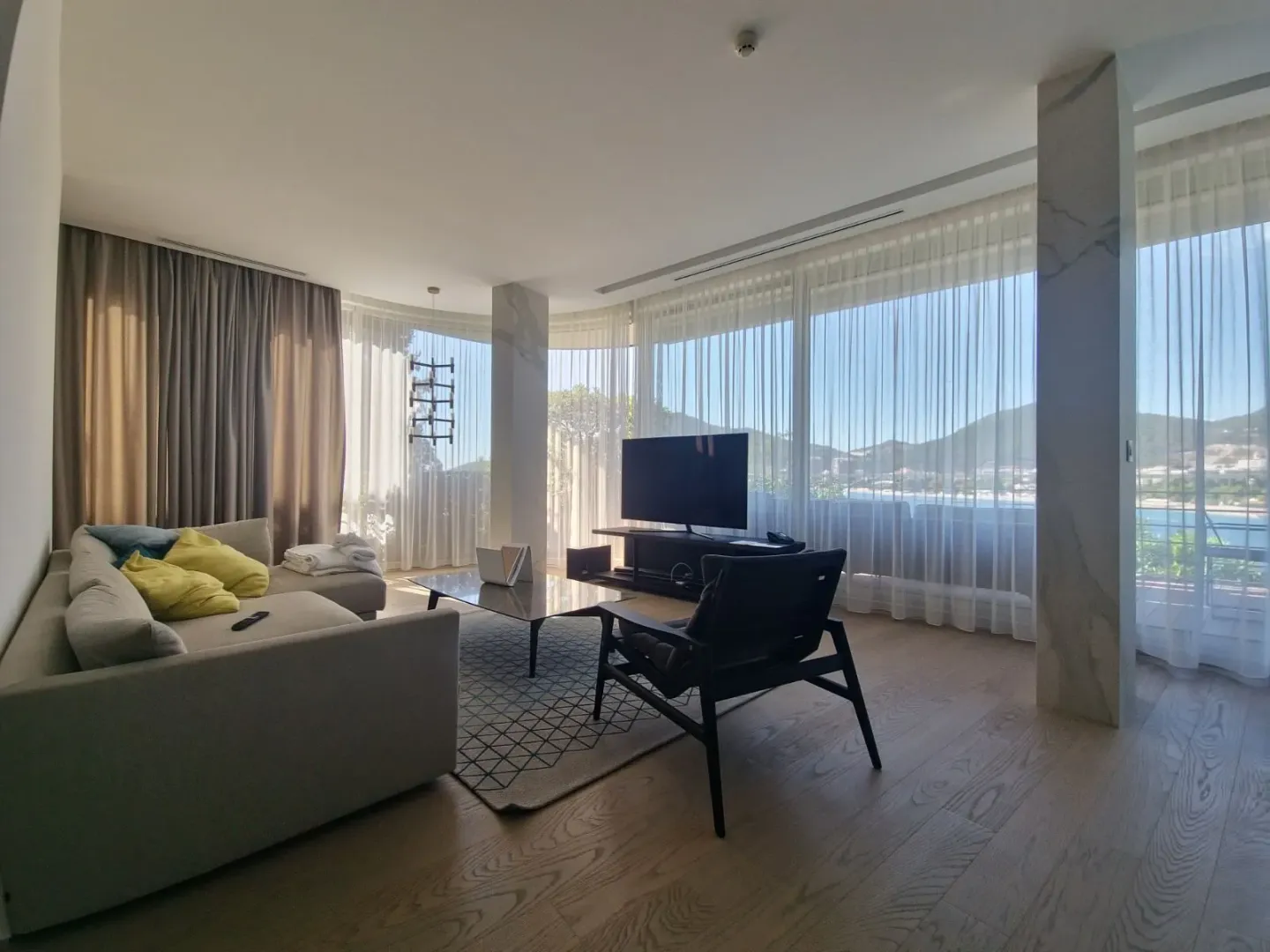 Living room with a sofa, TV, and large glass surfaces with a view.