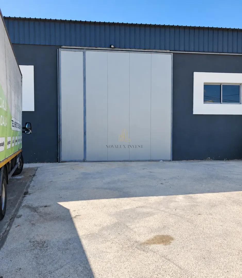 Exterior view of an industrial building with large sliding doors and a driveway.